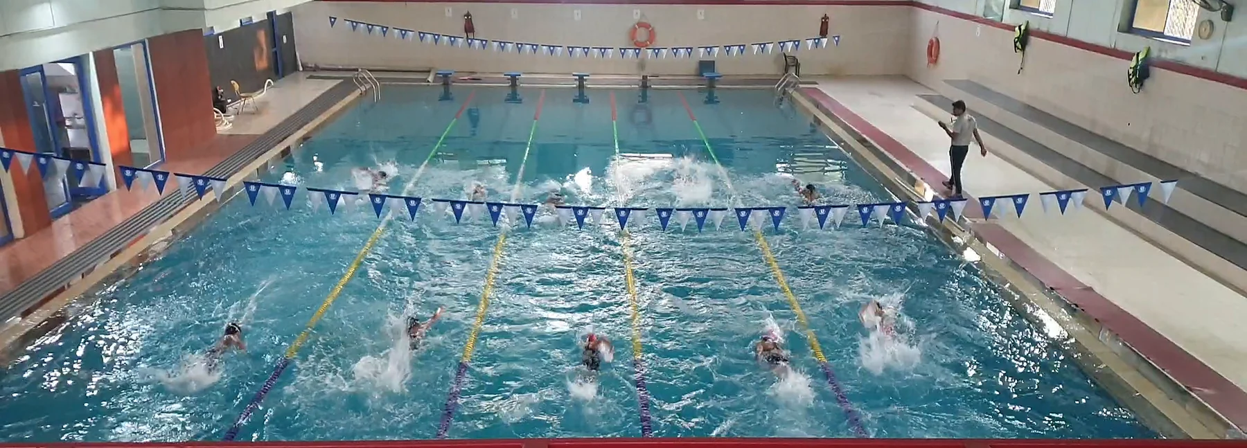 Swimmers mid-stroke in the lanes of the indoor pool, seen from the gallery