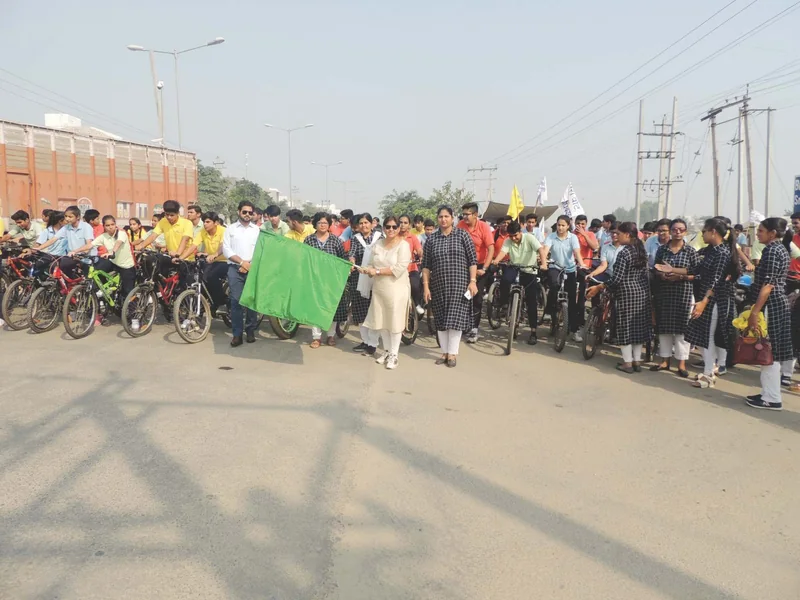 Students on bicycles at the start of an awareness rally, a teacher waving the green flag