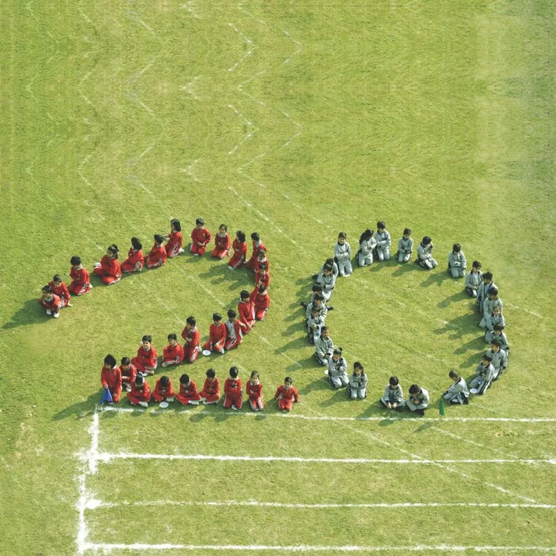 Students seated on the field in the shape of the number twenty, seen from above